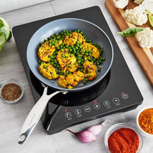 Black induction cooktop with skillet heating peas and chicken, white touch buttons