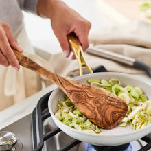 Cream skillet on gas stove with sliced onions and herbs; gold-tone handles