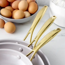 Cream skillet set with gold-tone handles near a bowl of eggs
