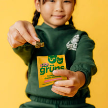 Child eating a green gummy while holding the Kids grüns pouch
