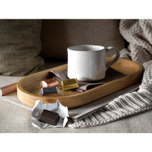 Assorted chocolate nuggets in wrappers on wooden tray with white mug and knit blanket