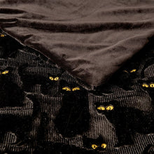 Black faux fur throw close-up with embroidered cat faces in yellow thread