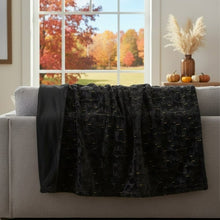 Black faux fur throw blanket with embroidered cat pattern, draped over couch