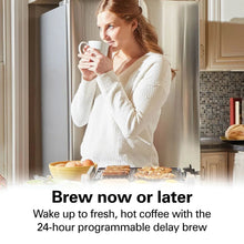 Coffee maker on kitchen counter beside mugs as a woman sips a cup of coffee