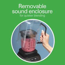 Blender jar with removable sound enclosure for quieter blending, shown with a hand.