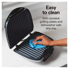 Indoor electric grill with open lid, grill plate being wiped with a cleaning cloth