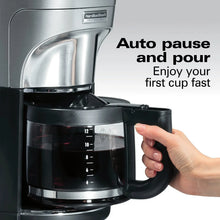 Stainless steel coffee maker with black carafe and lid, hand ready to pour
