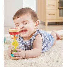 Rainbow bead shake rattle in infant hands, clear tube with red cap and teal base