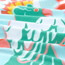Beach towel fabric close-up with green and teal bird shapes on light blue