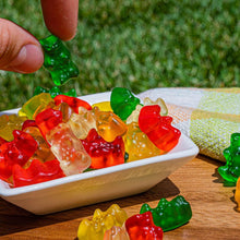 Gummy bears in a white tray, assorted red, green, yellow candies outdoors