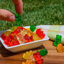 Assorted gummy bears in a serving bowl with a hand picking a green bear