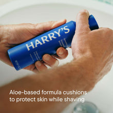 Hands holding Harry's foaming shave gel bottle with blue cap, label close-up