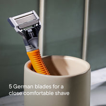 Orange handled 5-blade shaving razor with black head resting in a shaving cup