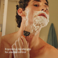 Blue-handled shaving razor held to chin with shaving foam