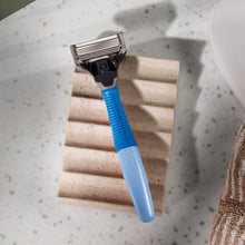 Blue-handled shaving razor with cartridge resting on a shower step