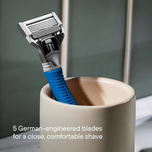 Blue-handled shaving razor with cartridge resting in a bathroom cup