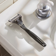 Men's razor with chrome head and textured black grip on sink ledge