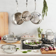 Stainless steel tri-ply cookware set with hanging ladles on a gas stove