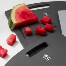 Dark gray cutting board with handle cutouts; watermelon wedge and diced fruit on top