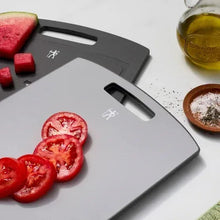 Light gray cutting board with handle cutout; tomatoes and herbs on the surface