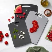 3-piece dark gray cutting boards with handle cutouts; watermelon, tomatoes, and herbs on boards