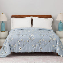 Light blue quilted blanket with scattered butterfly and flower print, folded over bed.