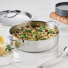 Stainless steel rondeau pot filled with herb and vegetable dish, with lid nearby