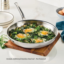Stainless steel skillet with lid, filled with sautéed greens and three sunny-side eggs.