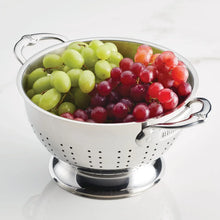 Stainless steel colander with perforations, filled with red and green grapes
