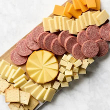 Assorted salami slices and yellow cheese wedges on a pale cutting board