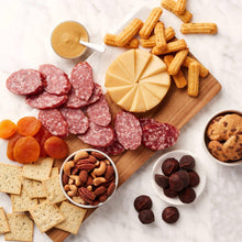 Assorted crackers, salami slices, cheese bites, cookies, and chocolate pieces on board