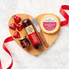 Wood heart charcuterie board with ribbon, sausages, Smoked Gouda wheel, and condiment jars