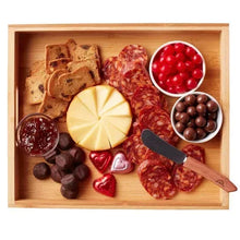 Wooden gift tray with slices of cheese, salami, crackers, berries, and chocolate pieces