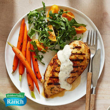 Ranch dressing topped grilled chicken with carrot sticks and mixed greens on a plate
