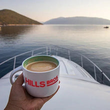 Hand holding a Hills Bros. mug with coffee on a boat