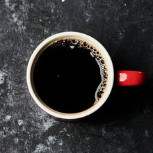White cup of dark coffee with crema, viewed from above on a dark surface.