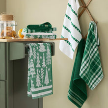 Set of green holiday kitchen towels on a cabinet, with tree and plaid designs.