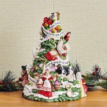 Christmas tree figurine with green foliage, red bells, and white figurines; soft LED glow