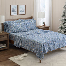 Holiday Market printed cotton sheet set in blue with winter sledding scenes, shown on a bed