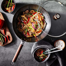 Carbon steel wok with glass lid over colorful stir-fry