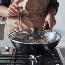 Carbon steel wok with glass lid and dark wood knob on stovetop