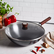 Carbon steel wok with glass lid and dark wood handle, on stovetop