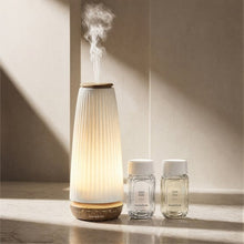 Lit ceramic diffuser with visible steam and two glass scent bottles on a ledge