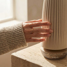 Hand adjusting a ribbed ceramic diffuser on a countertop with a wooden base