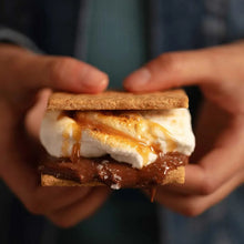 Hand holding a layered graham cracker sandwich with cream and caramel filling