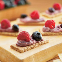 Graham cracker topped with creamy frosting and berries on a wooden board