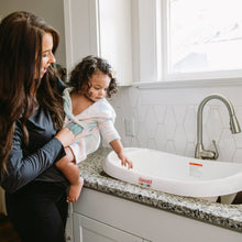 White 3-in-1 baby bathtub with sling insert, caregiver holding a child