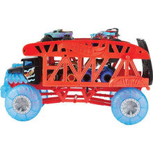 Red monster truck hauler carrying monster trucks with blue oversized wheels visible