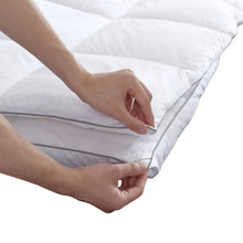 White feather bed topper corner being tucked under with hands