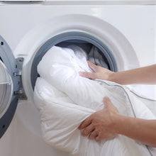 White feather bed topper going into a front-loading washing machine